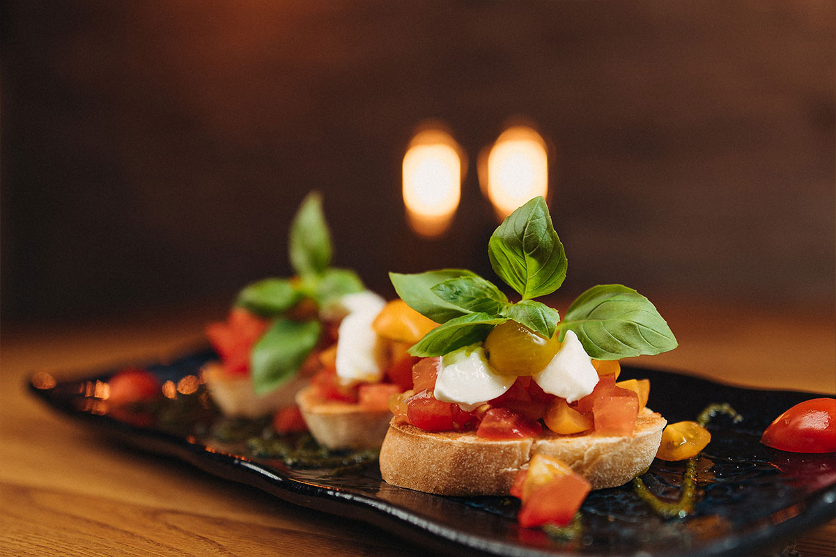 Bruschetta caprese mit bunten Cocktailtomaten, Mozzarella, frischem Basilikum und Olivenöl
